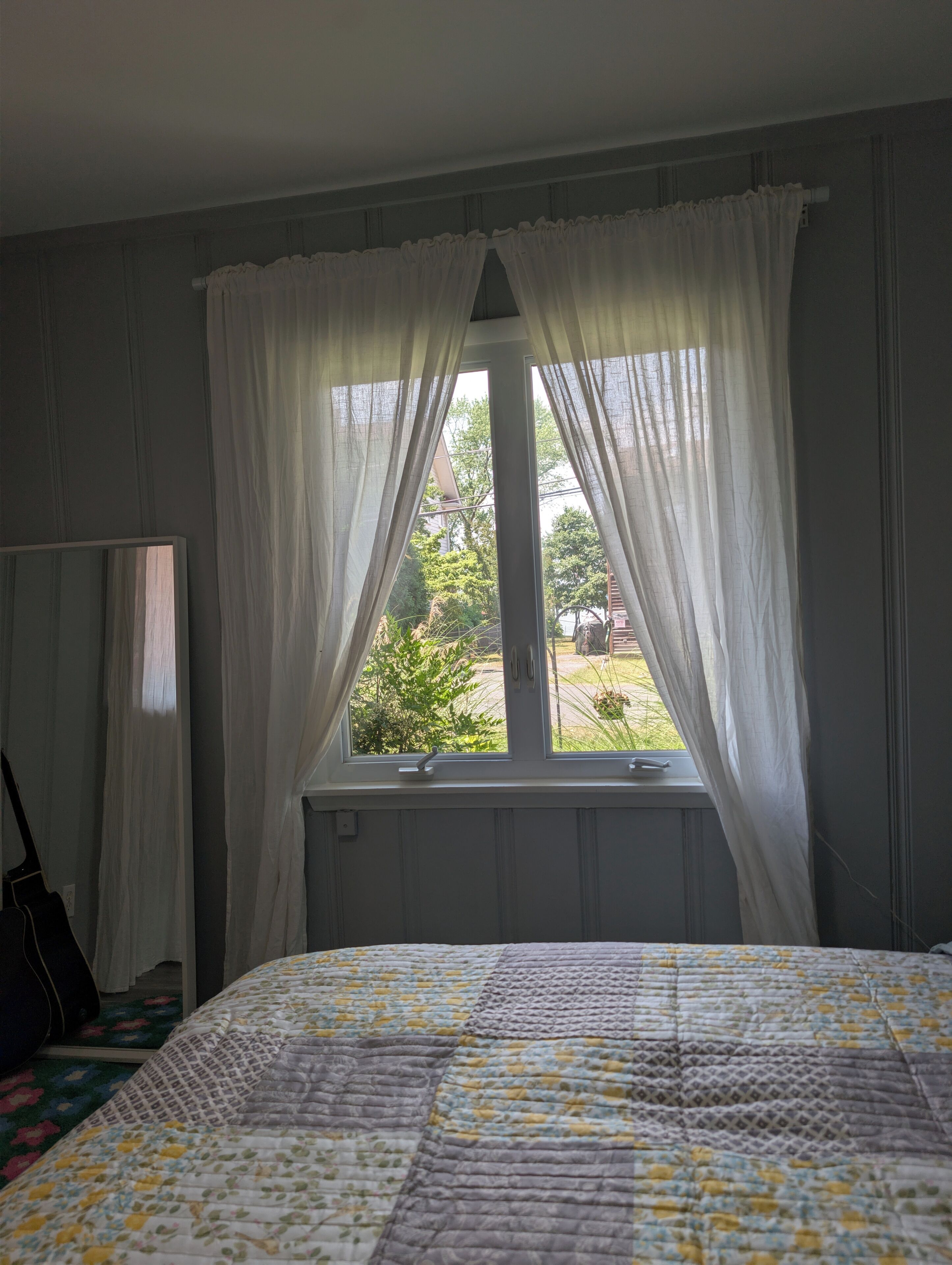Une chambre à coucher avec un lit, une fenêtre avec des rideaux, un radiateur et un miroir.