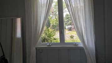 Een slaapkamer met een bed, een raam met gordijnen, een radiator en een spiegel.