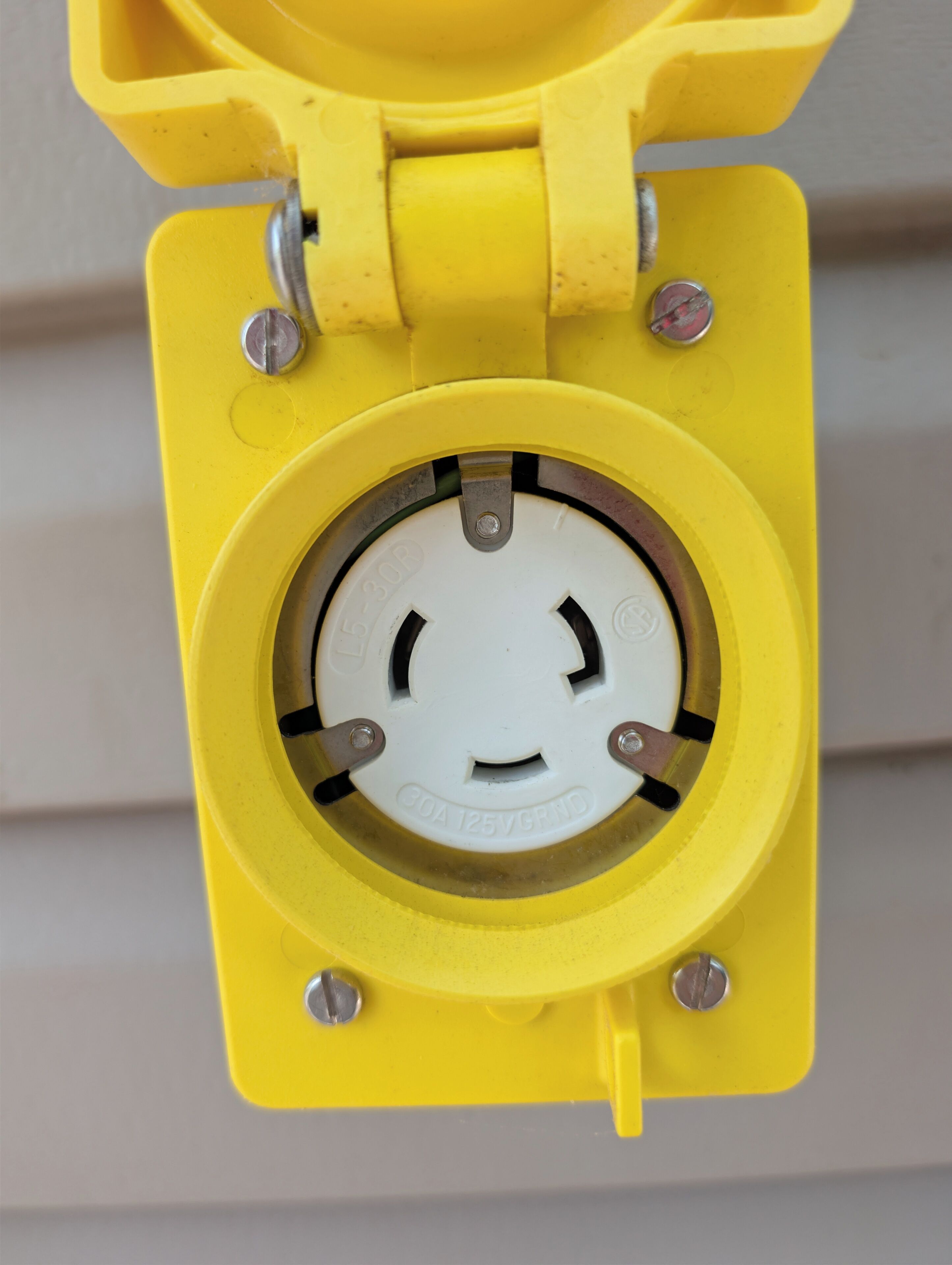 Une boîte électrique jaune, dotée d’un composant circulaire, de vis apparentes et d’un loquet métallique.
