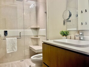 A modern bathroom with a glass shower enclosure, a toilet, a sink with a mirror, and a small plant on the countertop. - apartment (Bucerías)