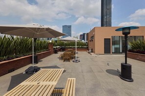 A rooftop patio with outdoor furniture, umbrellas, and a modern building in the background. - Studio · Private balcony, parking, rooftop & BBQ (Ciudad de México)