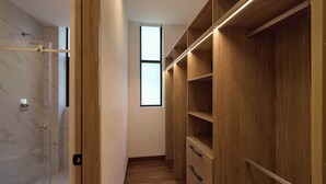 Un vestidor con estantes y cajones de madera, una puerta de ducha de cristal y un ventanal que proporciona luz natural.