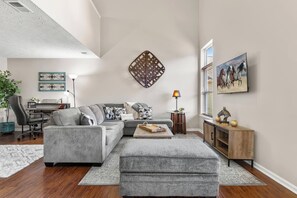 Ein modernes Wohnzimmer mit einem Ecksofa, einem Couchtisch, einem Schreibtisch und einer Lampe.