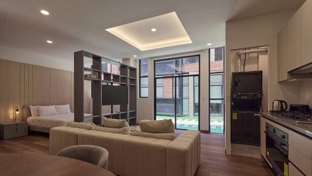 Un salon moderne comprenant un canapé, un lit, un téléviseur et un coin cuisine avec une cuisinière et un four.