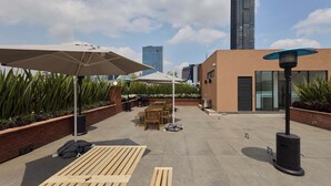 Una terraza en la azotea con mobiliario exterior, sombrillas y un edificio moderno al fondo.