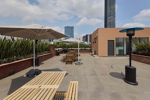 Eine Dachterrasse mit Gartenmöbeln, Sonnenschirmen und einem modernen Gebäude im Hintergrund.