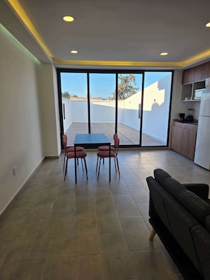 A spacious living area with a sliding glass door leading to a balcony, a dining table with chairs, a sofa, and a kitchenette. - Modern 1-Bed Apartment in Miguel Hidalgo with Balcony (Ciudad de México)