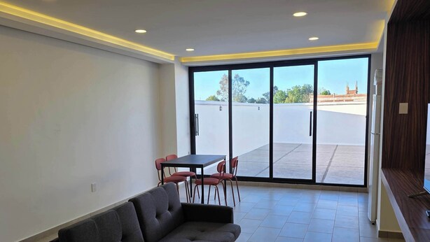 A modern living room with a sectional sofa, a dining table with chairs, and large sliding glass doors leading to an outdoor area. - Modern 1-Bed Apartment in Miguel Hidalgo with Balcony (Ciudad de México)