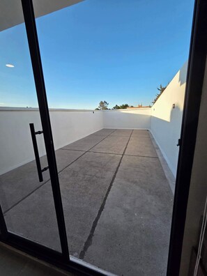 A clear view of a rooftop terrace with a concrete floor, white walls, and a clear blue sky. - Modern 1-Bed Apartment in Miguel Hidalgo with Balcony (Ciudad de México)