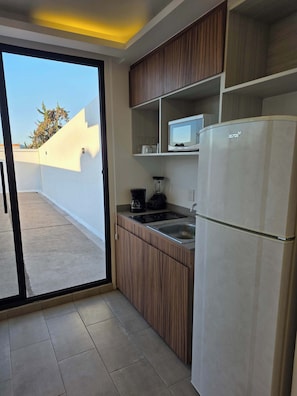 A modern kitchen with wooden cabinets, a built-in microwave, a refrigerator, and a sliding glass door leading to an outdoor area. - Modern 1-Bed Apartment in Miguel Hidalgo with Balcony (Ciudad de México)