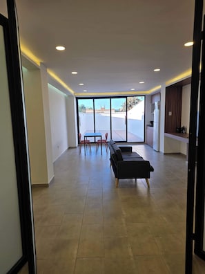 A spacious living area with a dining table and chairs, a sofa, and a kitchen area with a refrigerator. - Modern 1-Bed Apartment in Miguel Hidalgo with Balcony (Ciudad de México)