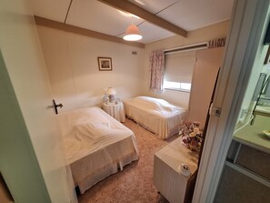 A small, cozy bedroom with two single beds, a bedside table with a lamp, a small picture on the wall, and a window with curtains.