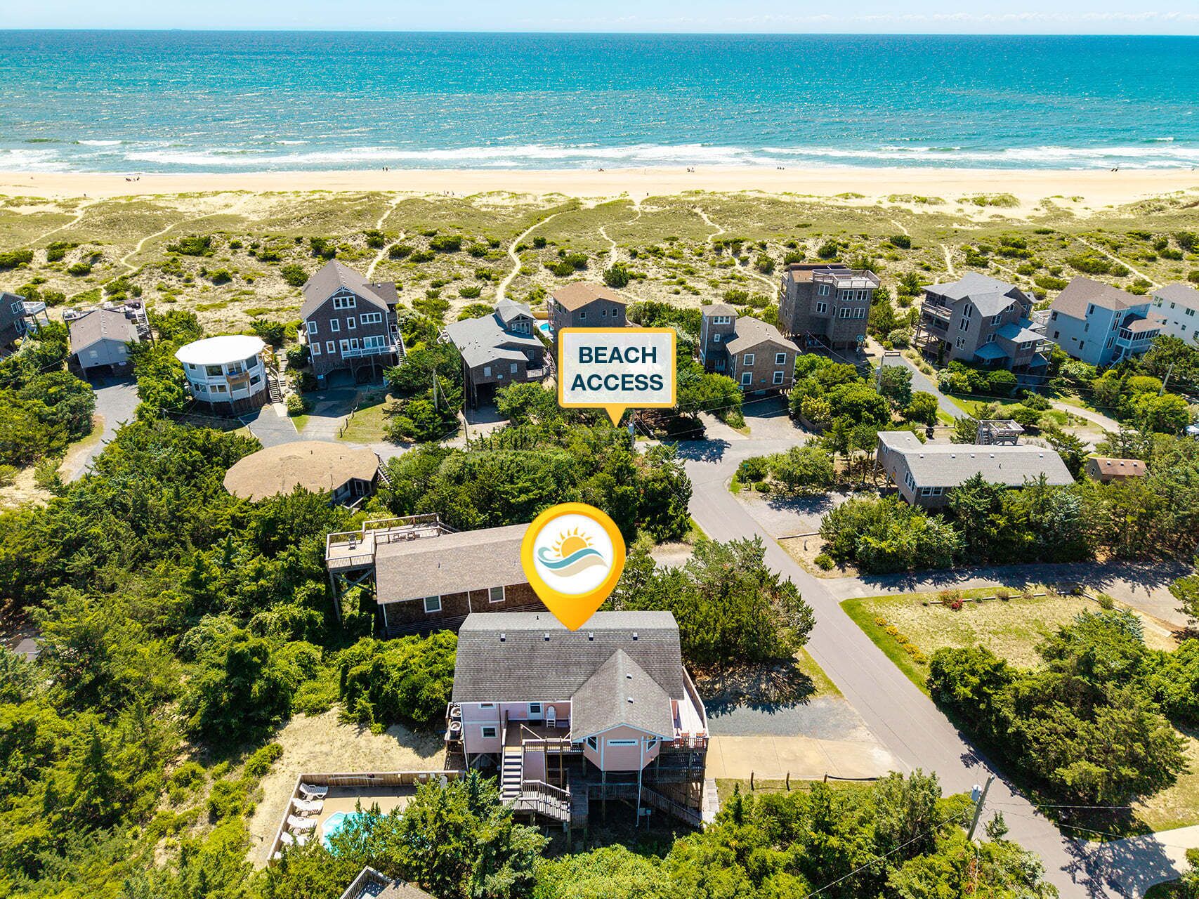 A coastal residential area with houses, a beach access sign, and a clear view of the ocean.