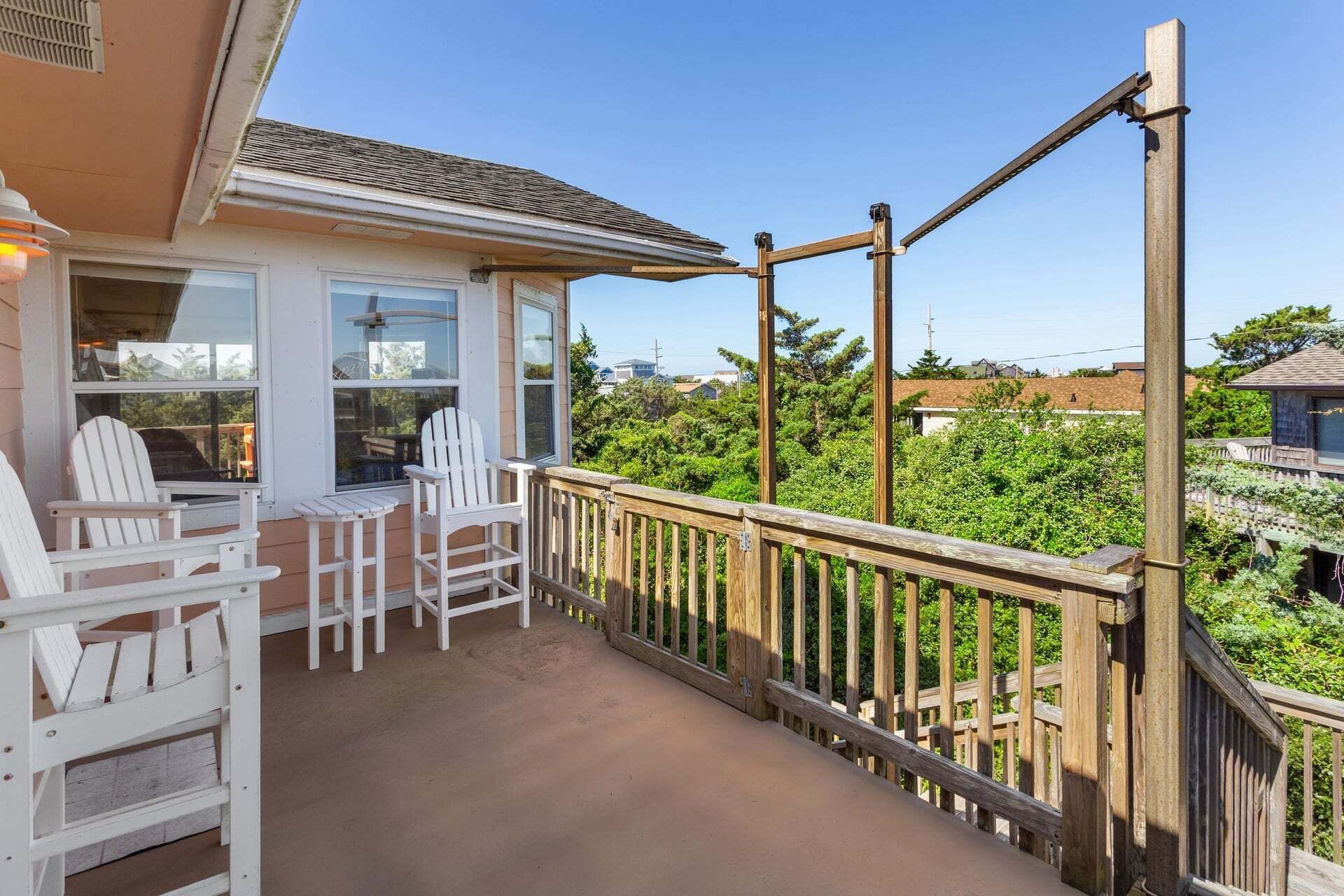 A covered porch with white Adirondack chairs, a wooden railing, and a view of a residential area.