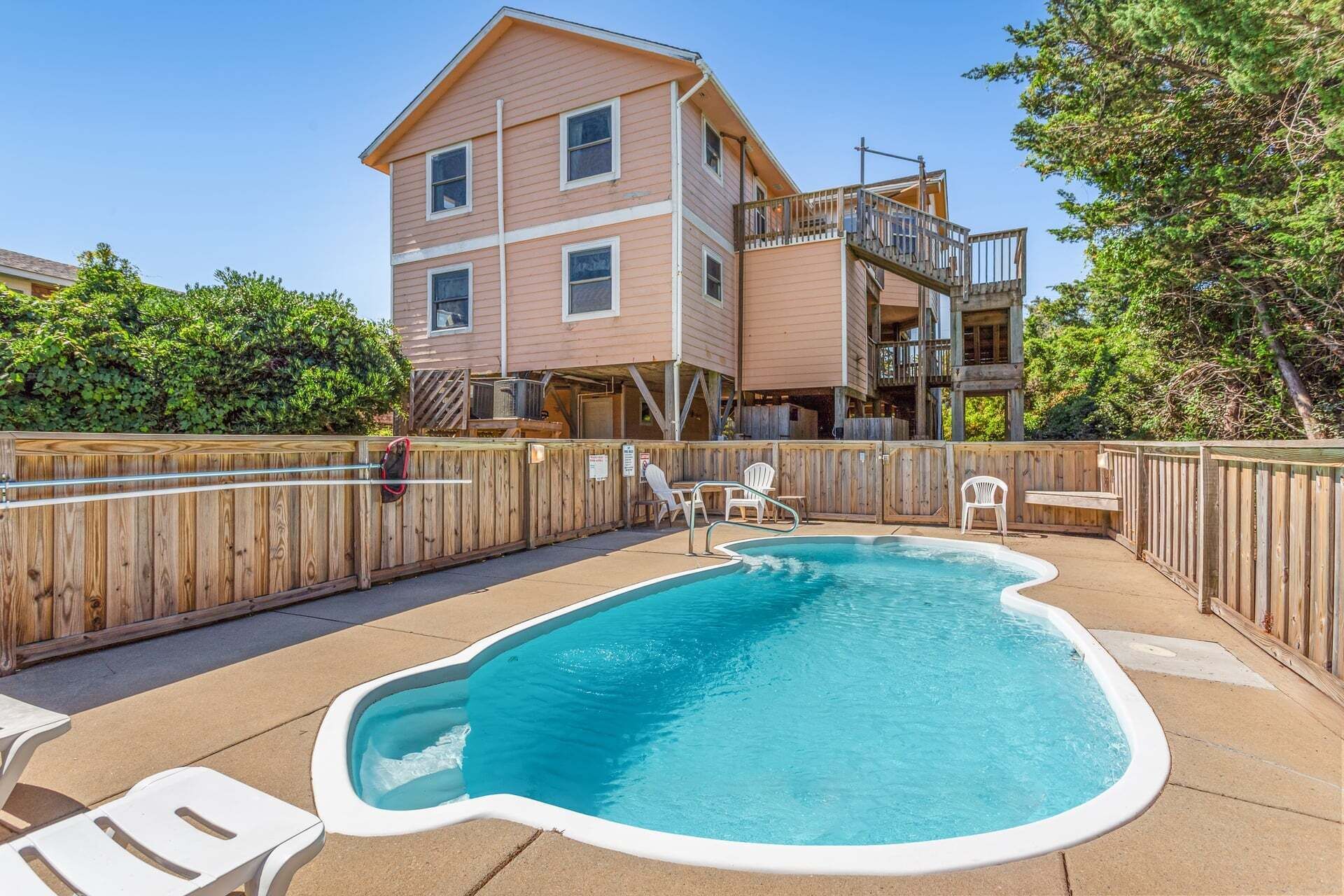 A two-story house with a backyard pool, wooden deck, and outdoor furniture.