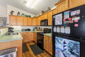 A kitchen with wooden cabinets, a black refrigerator, a microwave, and a stove. - Only a 2 minute walk to the Avon beach! Private Pool, Hot Tub, Luggage Lift (Avon)