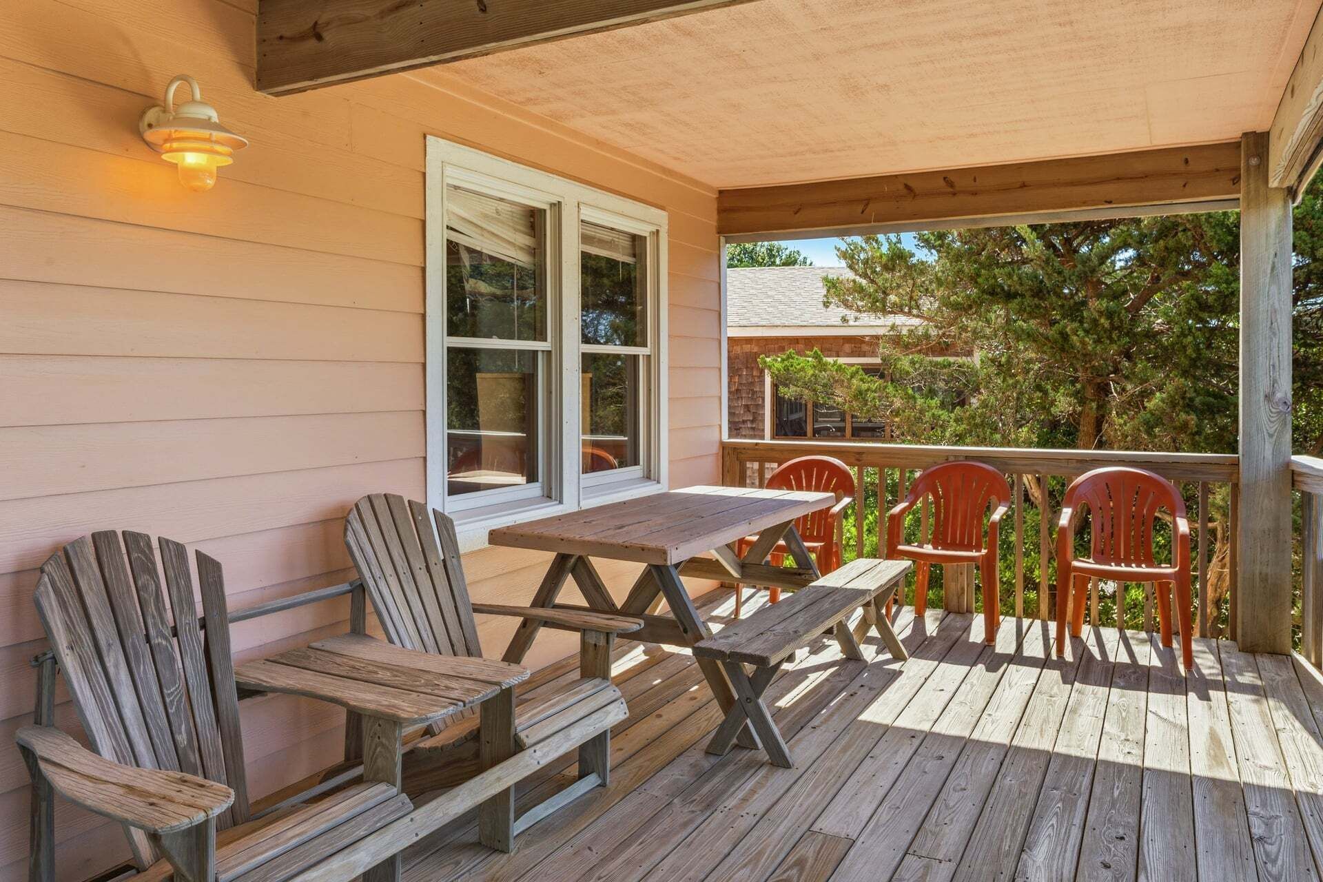 A wooden deck with a table and chairs, a window, and a light fixture.
