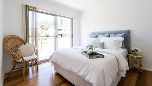 A bedroom with a large bed, a wicker chair, a small round side table, and a view through a sliding glass door. - Summer House - A stylish coastal retreat in Shoal Bay (Shoal Bay)