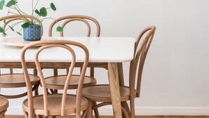 Ein Esstisch mit sechs Holzstühlen, einem Blumentopf und einer weißen Tischdecke.