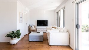 Ein modernes Wohnzimmer mit Flachbildfernseher, einem weißen Sofa, einem weißen Sessel und Holzboden.