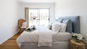 Ein Schlafzimmer mit Bett, Stuhl, kleinem Tisch und Blick durch ein Fenster.