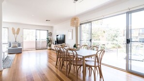 Ein großzügiger Wohnbereich mit Esstisch, Stühlen und einer Couch. Ein großes Schiebeglasfenster führt zu einem Außenbalkon.