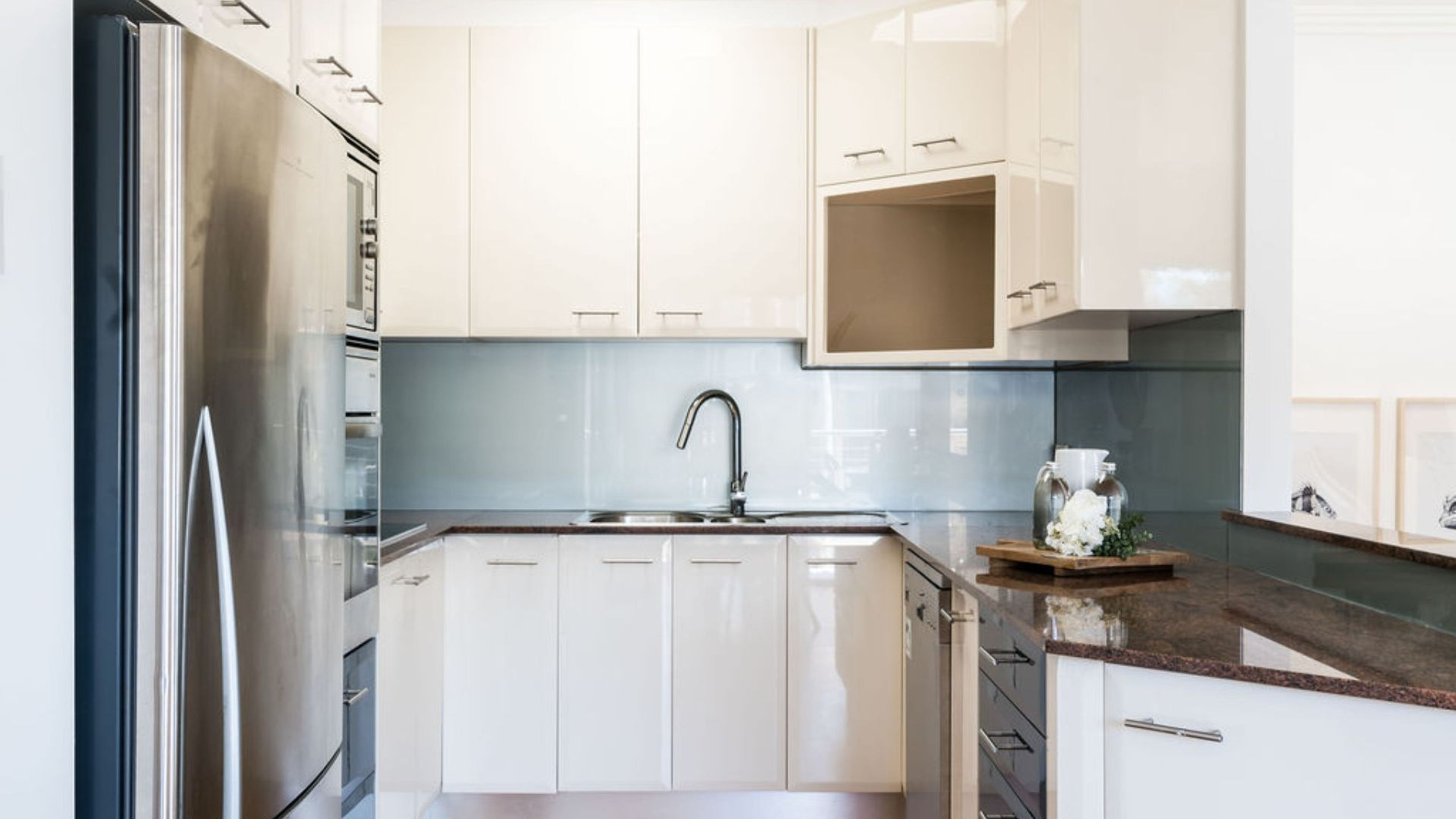 Eine moderne Küche mit weißen Schränken, einem Edelstahl-Kühlschrank und einer Arbeitsplatte aus Granit.
