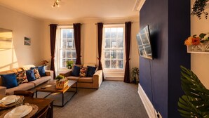 Een woonkamer met een bank, een salontafel en een aan de muur bevestigde televisie.