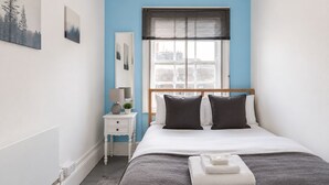 Een slaapkamer met een bed, nachtkastje, lamp en een raam met zonwering.