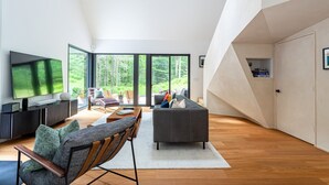Una sala de estar moderna con un televisor grande, asientos cómodos y vistas a un bosque a través de amplios ventanales.