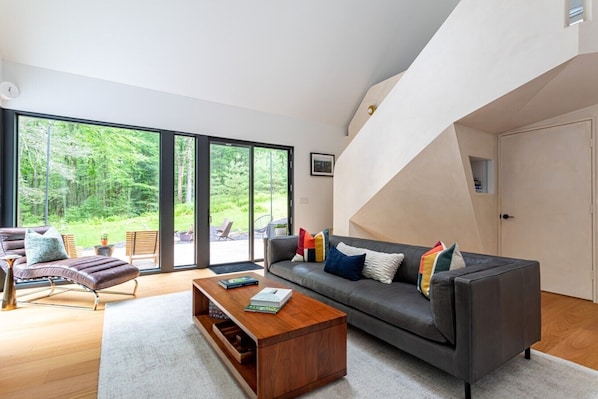 Un salon moderne avec un canapé, un fauteuil et une table basse, de grandes fenêtres et un escalier.