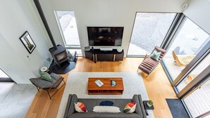 Una sala de estar moderna con sofá, mesa de centro, televisión, chimenea y ventanas amplias.