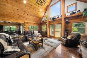 A spacious log cabin interior with a large living area, leather furniture, and a high ceiling. - Spacious Cabin Retreat with Hot Tub & Game Room (Sugar Grove)