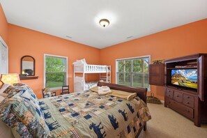 Ein Schlafzimmer mit Etagenbett, Fernseher, Schreibtisch und einem Fenster mit Jalousien.