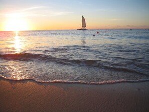 Ein Strand mit sanften Wellen, einem Segelboot und einem Sonnenuntergang.
