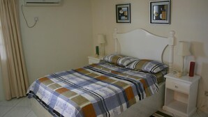 Ein Schlafzimmer mit einem Bett, zwei Nachttischen, einer Ablage und einer Klimaanlage, sowie zwei gerahmten Bildern an der Wand.