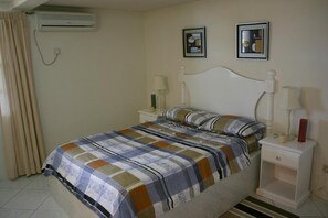 Een slaapkamer met een bed, twee nachtkastjes, een airconditioning en twee ingelijste foto’s aan de muur.