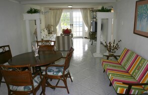 Een eetgedeelte met een ronde tafel en stoelen, een gestreept sofa, en uitzicht op de omgeving door een raam.