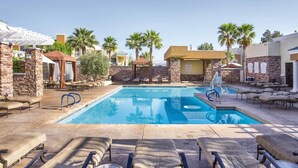 Un espace piscine comprenant des chaises longues, une piscine et des palmiers.