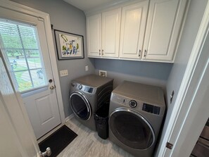 A laundry room with two front-loading washing machines, white cabinets above, a door with a window, and a small rug at the entrance.
