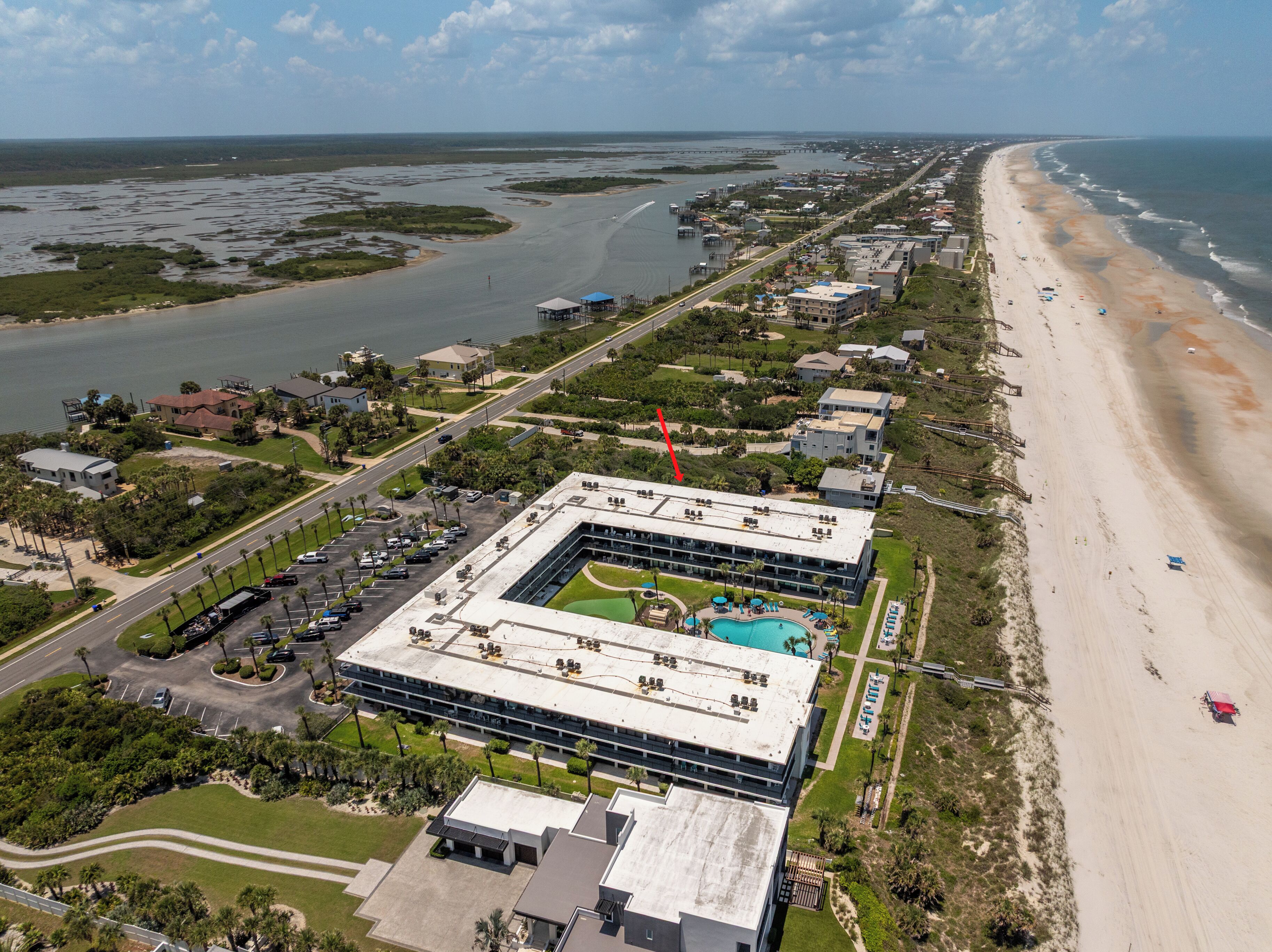Ein Luftbild eines Küstenhotels mit Schwimmbad, angrenzendem Strand und einer Marina.