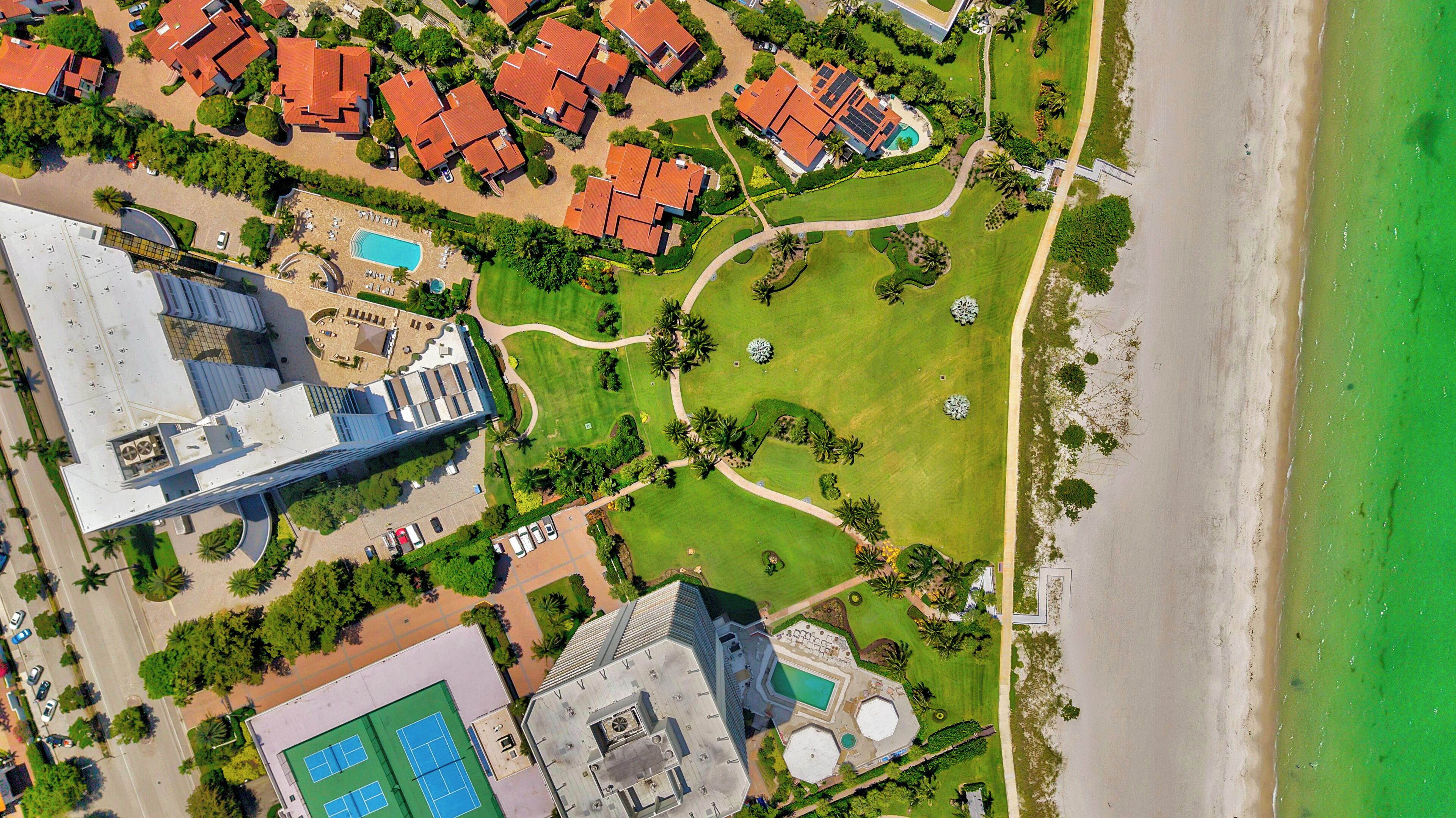 An aerial view of a coastal area with a large building, a beach, and a golf course.