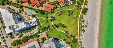 An aerial view of a coastal area with a large building, a beach, and a golf course.