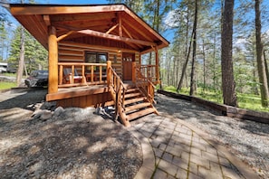 Eine Blockhütte mit Veranda, Holzstufen und einem Schotterweg.