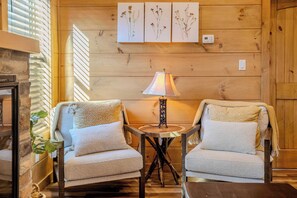 A cozy room with two armchairs, a small table with a lamp, wooden walls, and a fireplace. - Smoky Escape - Private Hot Tub - Near The Island (Pigeon Forge)