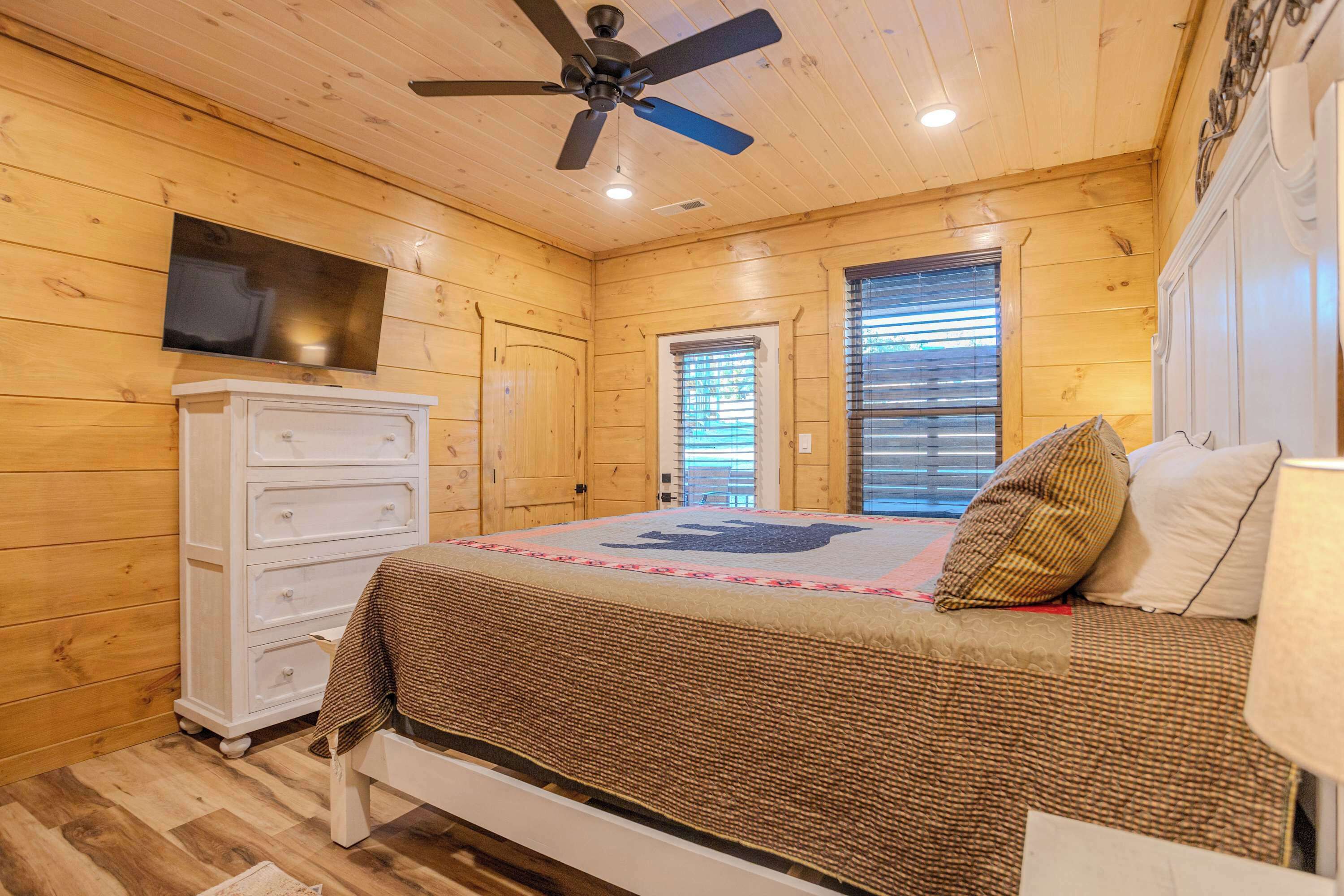 A wooden-paneled room with a bed, dresser, ceiling fan, and a TV mounted on the wall.