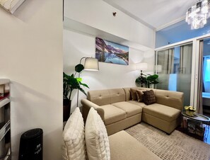 A living room with a beige sectional sofa, two floor lamps, a large painting, and a glass door leading to a balcony. - Cebu Sweet Staycation (Cebu City)