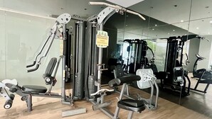 Ein Fitnessraum mit unterschiedlichen Trainingsgeräten, einem Warnschild und Holzboden.