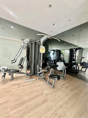 A gym with various exercise machines, a caution sign, and a wooden floor. - Cebu Sweet Staycation (Cebu City)