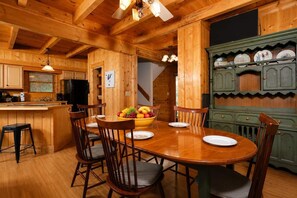 A wooden interior with a dining table, chairs, a fruit bowl, and a kitchen area with cabinets. - Chalet Escape | Pet Friendly • Pool • Hot Tub! (Gatlinburg)
